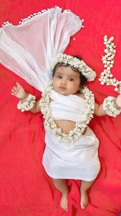 a baby dressed in white laying on top of a red blanket