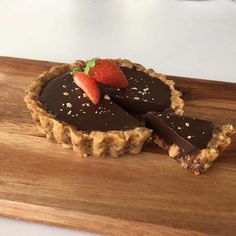 a chocolate tart with a strawberry on top sits on a wooden cutting board, ready to be eaten