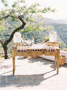 a wooden table topped with lots of glasses and bottles on top of a stone floor