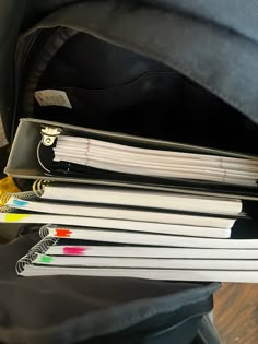 several folders and pens are stacked on top of each other in an open backpack