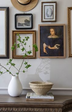 there are many framed pictures on the wall above a table with a vase and flowers in it