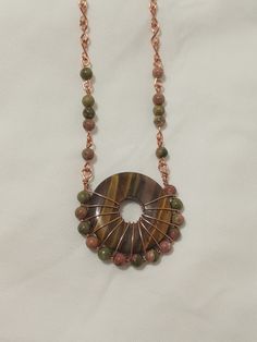 Every inch of this necklace is handmade, it is totally unique even down to the chain. Made with copper wire, a beautiful Tigerseye stone, and high quality Unakite beads. The pendant is 1 1/2 x 1 1/2 inches, and the chain is 20 inches, with a hook and eye clasp. Handmade Unique Wire Necklaces, Unique Handmade Wire Necklaces, Handmade Round Earthy Necklaces, Handmade Earthy Round Necklaces, Handmade Round Earthy Necklace, Earthy Copper Pendant Necklace, Artisan Copper Necklaces With Gemstone Beads, Artisan Copper Necklace With Gemstone Beads, Bohemian Brown Copper Wire Jewelry