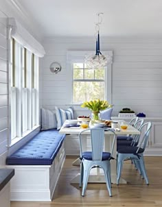 a dining room table with blue chairs and a bench in front of the window,