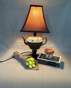 a table lamp sitting on top of a table next to a bag of grapes and a book