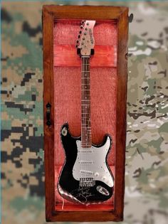 an electric guitar in a wooden case on a camo wallpapered background,