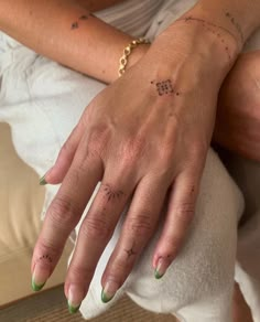 a woman's hand with green nail polish and tattoos on her left arm, sitting on a bed