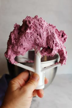 a hand holding a mixer with pink frosting in it