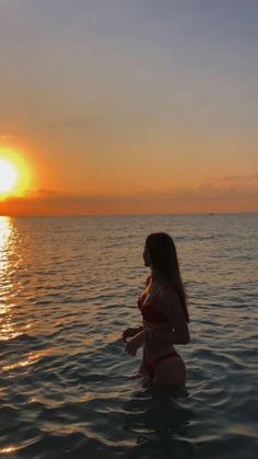 a woman standing in the water at sunset