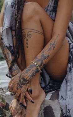 a woman with tattoos on her arm and leg sitting next to a body of water