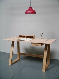 a wooden desk with two drawers underneath a red light hanging from the ceiling above it