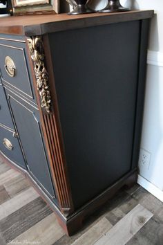 a black cabinet with gold decorations on the top and bottom, next to a white wall