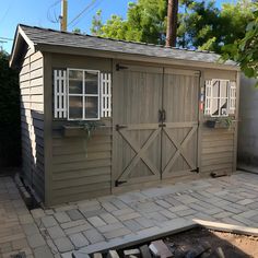 an outdoor storage shed with the doors open and brick walkway leading up to it's entrance