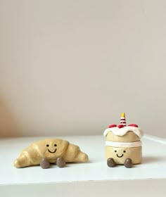 two small clay animals sitting next to each other on a white counter top, one with a birthday hat and the other has a smiling face