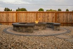 an outdoor fire pit surrounded by rocks and gravel with a wooden fence in the background