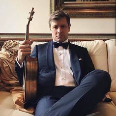 a man in a tuxedo sitting on a couch holding a guitar