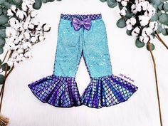 a blue and purple mermaid outfit with a bow on the side, next to cotton flowers