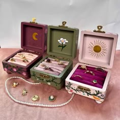 four different colored boxes with jewelry in them on a pink cloth covered surface, one is open and the other two are closed