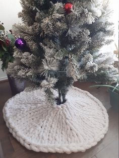 a white christmas tree skirt on top of a round rug in front of a potted plant