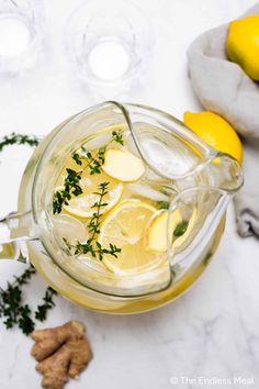 a pitcher filled with lemonade next to some sliced lemons and ginger florets