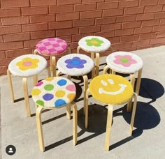 four stools with smiley faces painted on them sitting in front of a brick wall