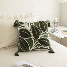 a green and white pillow sitting on top of a bed next to a table with a lamp