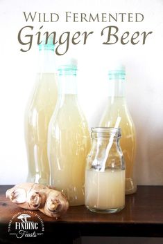 three glass bottles filled with ginger beer sitting on top of a wooden table next to sliced ginger