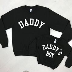 We can't even deal with the cuteness of these Daddy & Daddy's Boy father & son matching sweatshirts. Add sizes into cart separately. Daddy & Daddy's Boy matching Classic styled sweatshirts Crew Neck College style text Ringspun cotton Wash at 30 Degrees Family Matching Graphic Print Sweatshirt, Father's Day Casual Sweatshirt With Name Print, Black Family Matching Tops For Winter, Family Matching Black Tops For Fall, Black Family Matching Tops For Fall, Family Matching Crew Neck Sweatshirt For Father's Day, Father's Day Cotton Sweatshirt With Name Print, Black Crew Neck Sweatshirt With Lettering, Black Long Sleeve Sweatshirt With Name Print