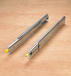 two metal brackets with yellow handles on a wooden surface, one is closed and the other has