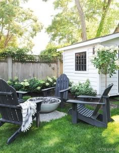 two adiron chairs sitting in the grass near a fire pit and potted plants