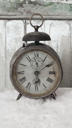 an old fashioned clock sitting on top of a white fur covered floor next to a window