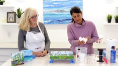 two women standing at a table in front of paintings