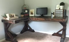 a wooden desk with a computer monitor and other items on it in front of a white wall