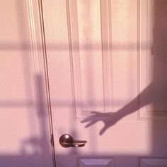 the shadow of a person's hand coming out of a door with a handle