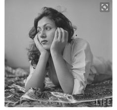 a woman laying on top of a bed next to a wall with her hands under her face