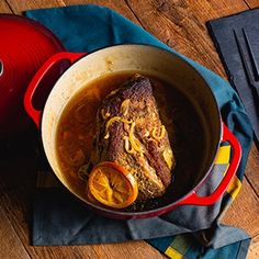 a red pot filled with soup on top of a wooden table next to a blue napkin