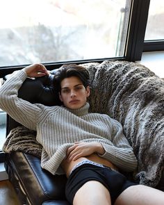 a young man laying on top of a couch next to a large dog in front of a window