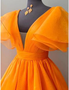 an orange dress on a mannequin with a gold necklace and earring hanging from the neck