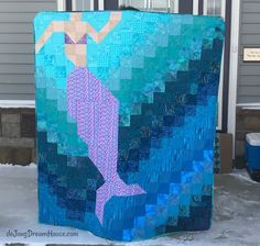 a blue and purple quilt with a mermaid on it's front porch in the snow