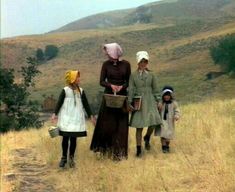 three women and two children are standing in a field with hills in the back ground