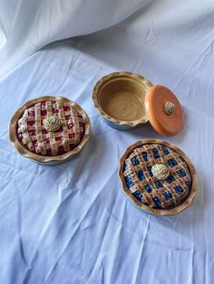 "Ceramic jars sculpted to look like pies. Comes in three \"flavors\" - Blueberry, Cherry and Pumpkin.  Blueberry Pie Jar features a gray \"aluminum pie tin\" base with a wavy \"pie crust\", the jar lid features blue \"berries\", a lattice \"crust\" and a \"whipped cream\"handle.  Cherry Pie Jar features a gray \"aluminum pie tin\" base with a wavy \"pie crust\", the jar lid features red \"berries\", a lattice \"crust\" and a \"whipped cream\" handle.  Pumpkin Pie Jar features a gray \"aluminum p Memory Box Ceramics, Clay Containers With Lids Ideas, Clay Jars With Lids, Clay Containers With Lids, Pie Pot Holder, Ceramic Lidded Jars, Pie Ceramic, Food Ceramics, Pie Jars