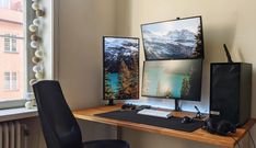 a computer desk with two monitors and a keyboard on it, in front of a window