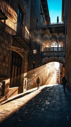 a person walking down an alley way in the sun with shadows on the pavement and buildings