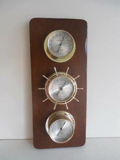 three clocks mounted to the side of a wooden plaque with ships wheels on each wall