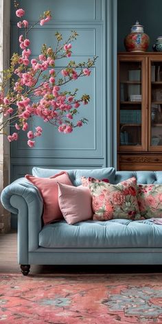 a living room with blue walls and pink flowers on the couch, rugs and bookshelves