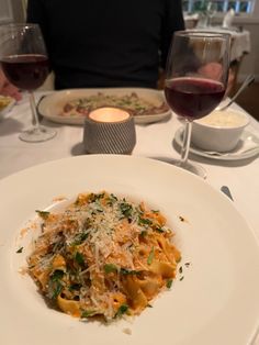 a white plate topped with pasta and cheese next to two glasses of wine on a table