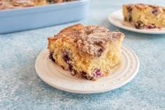 a piece of blueberry coffee cake on a white plate next to a baking dish