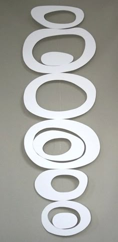 a group of white circles hanging from the ceiling in front of a gray wall with a clock on it's side