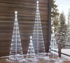 three lighted christmas trees sitting on top of a wooden deck