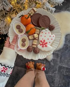 a person holding a plate with cookies and candies on it next to a christmas tree