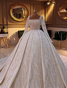 a white wedding gown on display in a room with mirrors and chairs behind the mannequin